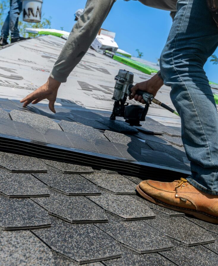 Roofer using nail gun for shingle installation on residential roof.